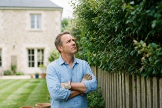 Homme regardant une haie trop haute dépassant la clôture de son jardin, illustrant les conflits de voisinage liés aux végétaux envahissants