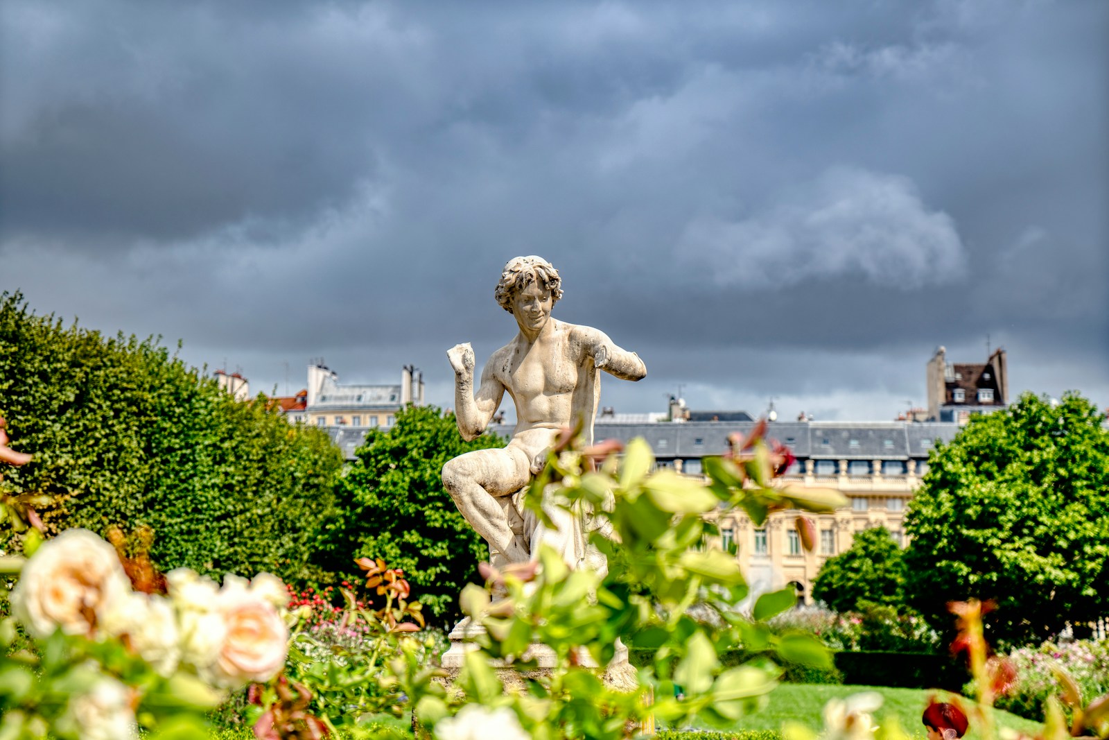 a statue of a person in a garden with buildings in the background